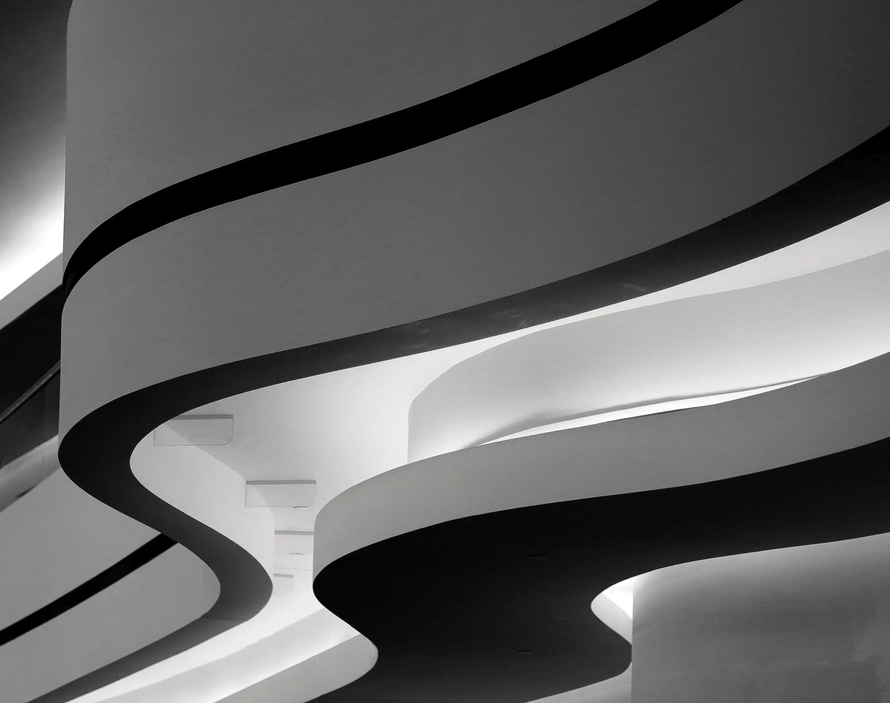 A closeup greyscale shot of a building with curvy twists in Berlin, Germany Moderne Treppenhaus-Architektur mit geschwungenem Design und indirekter Beleuchtung, symbolisiert innovative Arbeitsumgebung bei Heinrich & Coll.